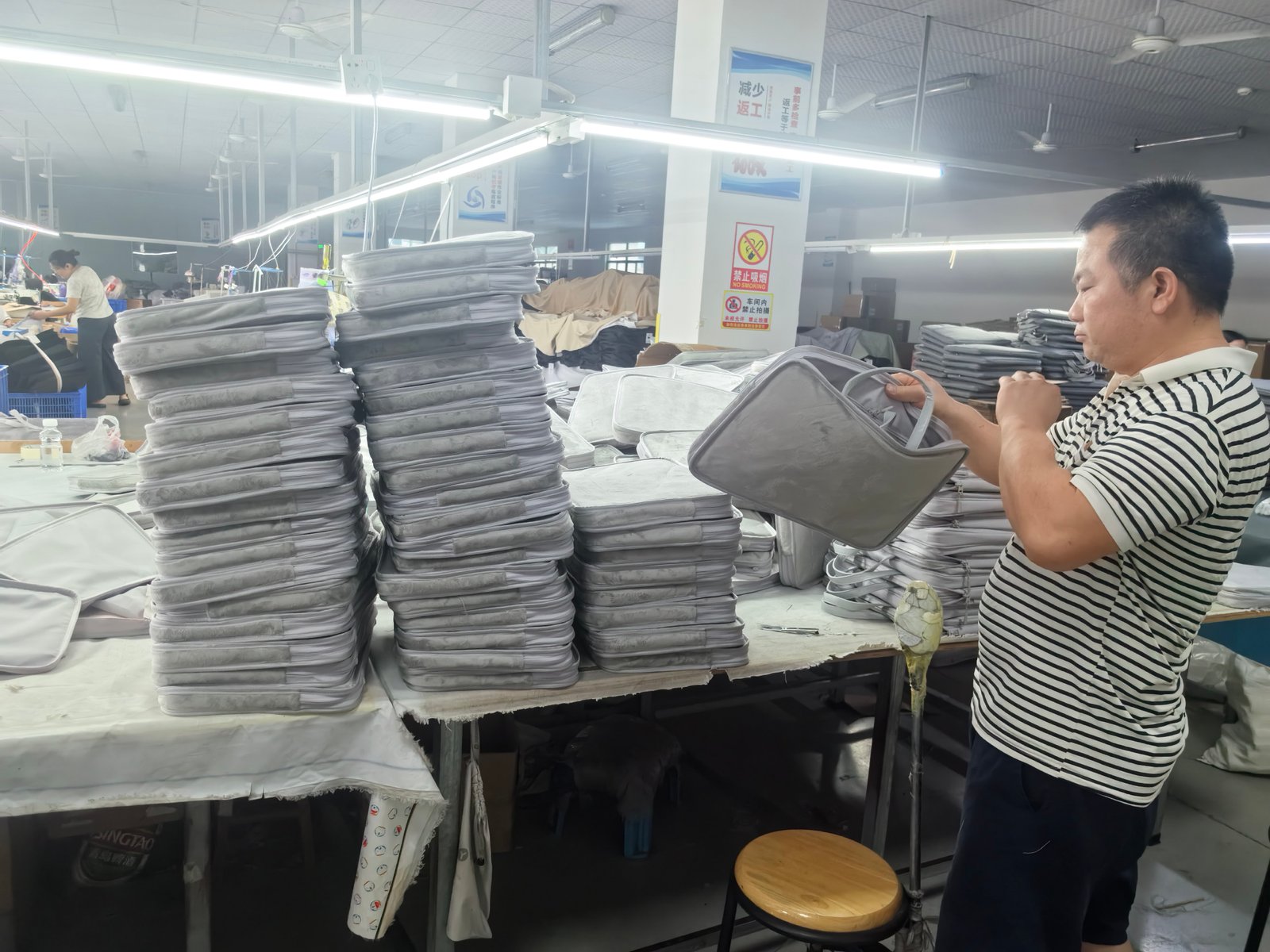 Yishu Bag team member checking a finished grey bag beside a production batch